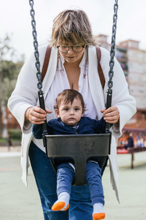 A mother playing with her little son in the swing in the playgroundの写真素材