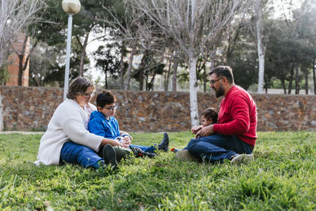 A loving family sitting on the lawn of a park playing with their children