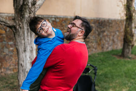 Man holding and playing with his son with disability while enjoying good time together outdoors.の写真素材