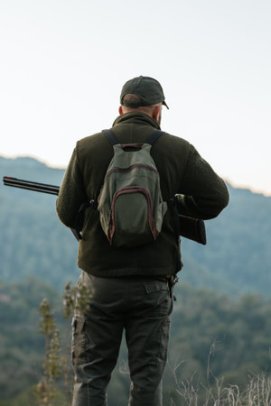 Back view of a hunter holding a shotgun while standing outdoors looking for prey.の写真素材