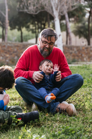 Father enjoying playing with his children sitting on the grass outdoors.の写真素材