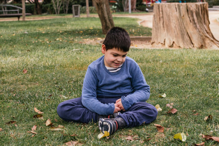 Child with disabilities enjoying outdoors while sitting on a grass in a park.の写真素材