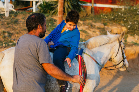 Child with disabilities doing an exercise during an equine therapy session with a physiotherapist.の写真素材