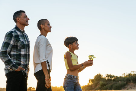 Young girl and her parents standing outdoors in the nature with a plant.の写真素材