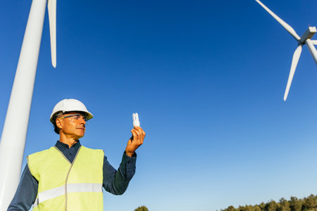 Male engineer holding a light bulb while standing in wind turbine field.