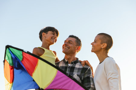 Happy family smiling while enjoying playing with a kite outdoors.の写真素材