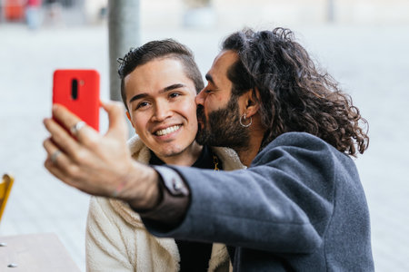 Man giving a kiss on the cheek to his boyfriend sitting in a restaurant.の写真素材