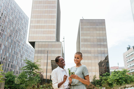 two women are smiling and having a good time while using a smartphone, they are businesswomen and in...