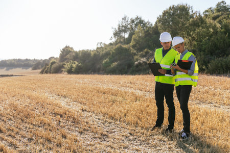 A team of engineers standing in the field looking at blueprints on a mobile phone.の写真素材