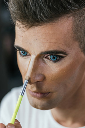 Gay man using a brush to making up his faceの写真素材