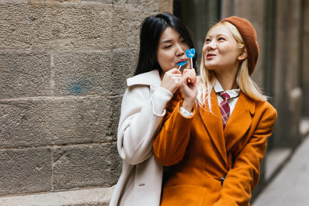 Asian lesbian couple eating lollipops while having a date outdoors.の写真素材