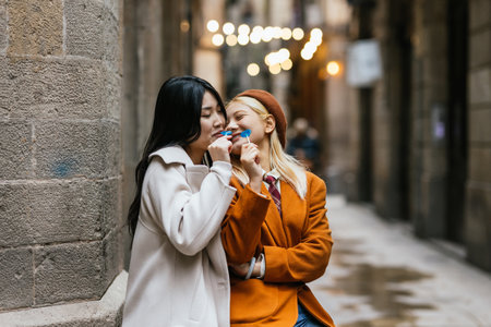 Lesbian couple eating lollipops standing close to each other outdoors.の写真素材
