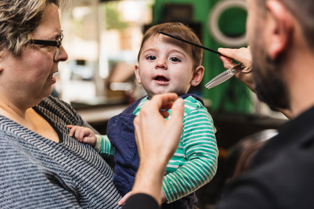 Young child looks curious while getting their haircut with a parent at a salonの写真素材