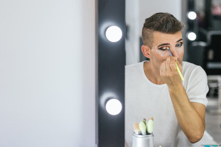 Man applying eyeshadow with makeup brush while preparing in the dressing room.の写真素材