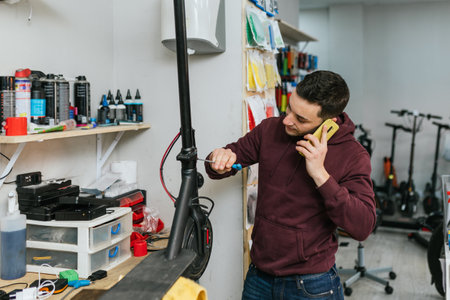 The bike mechanic attends a call while repairing an electric scooter with a screwdriver.の写真素材