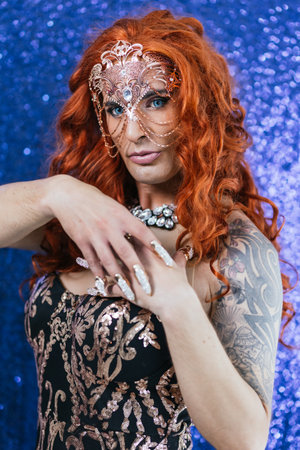 Stylish drag queen artist wearing a mask while posing on a glitter background.の写真素材