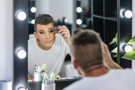 Man applying mascara on eyelash while doing his makeup in a dressing room.の写真素材
