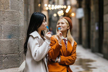 Asian lesbian couple eating lollipops outdoors on the street.の写真素材