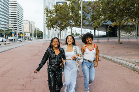 Three joyful friends walking together on a city street during early evening.の写真素材