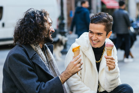 Two men sitting on the street eating ice cream conesの写真素材
