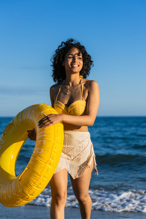 Happy young woman enjoying a sunny summer day at the beach with a yellow inflatable ring, embodying carefree vacation vibesの写真素材