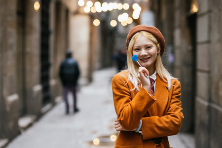 Asian woman smiling while eating a lollipop outdoors on the street.の写真素材