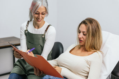 Microblading technician discusses the process with a smiling client seated in a salonの写真素材