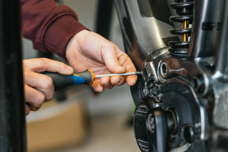 Detail shot of the hands of a bike mechanic using a screwdriver to manipulate and unscrew the electrical system of an electric mountain bike.の写真素材