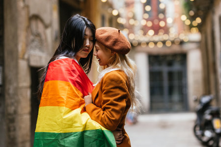 Lesbian couple with the rainbow flag while standing close to each other on the street in Barcelona.の写真素材