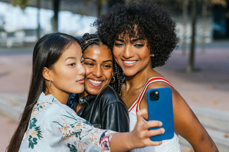 Female friends sharing a joyful selfie moment in an urban setting at dusk.の写真素材