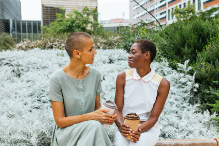 Two Friends Sharing a Moment Over Coffee in a Lush Parkの写真素材