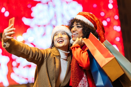 Two happy friends taking selfie while holding shopping bags in christmas nightの写真素材