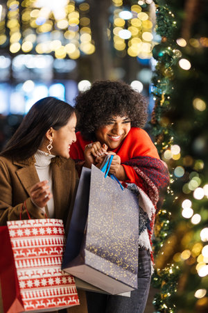 Two happy young women enjoying christmas shopping in the city at nightの写真素材