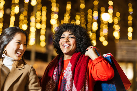 Two happy women holding shopping bags enjoying christmas shopping at nightの写真素材