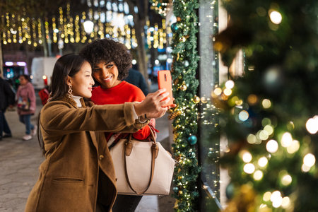 Two young women taking selfie in christmas decorated city at nightの写真素材