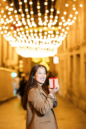 Young woman holding christmas gift on decorated city street at nightの写真素材