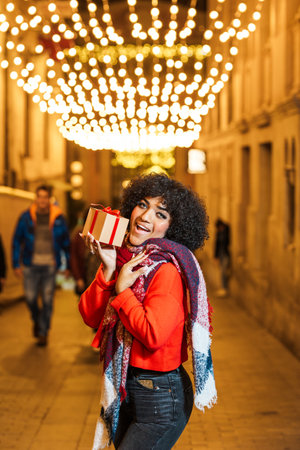 Young woman holding christmas present on decorated shopping streetの写真素材