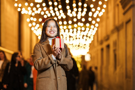 Young woman holding christmas present on decorated streetの写真素材