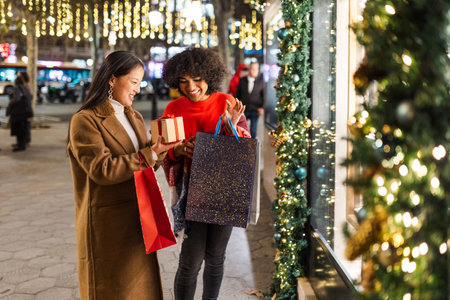 Two young women are having fun while going christmas shopping at night in a decorated cityの写真素材