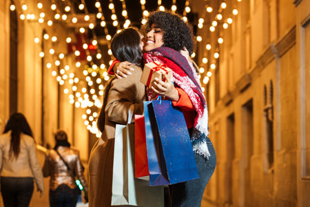 Two happy women holding christmas gifts are hugging in a decorated streetの写真素材