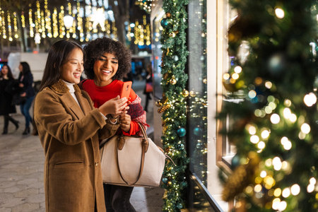 Two friends taking a selfie in front of a christmas shop window displayの写真素材