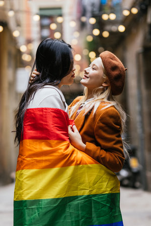 Interracial lesbian couple embracing and holding lgbt flagの写真素材