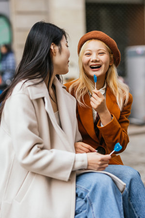 Two women sitting down, one with a bluelollipop in her mouth and the other smilingの写真素材