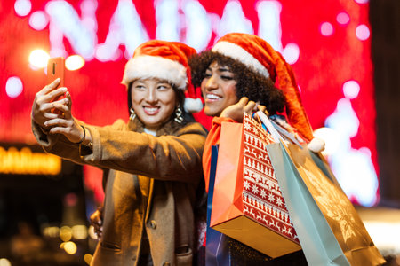 Two girls taking selfie holding shopping bags during christmas timeの写真素材