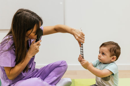 Female optometrist performing retinoscopy exam on toddler boy using retinoscopeの写真素材