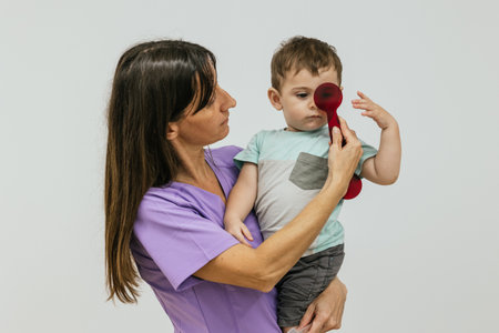 Female optometrist checking eyesight of baby boy patient holding red measuring instrumentの写真素材
