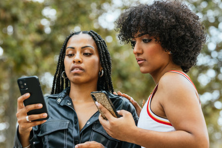Two girls using smartphones outdoors in a parkの写真素材
