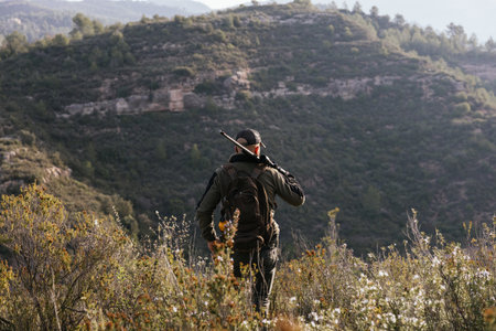 Hunter walking on a mountain ridge carrying a rifle