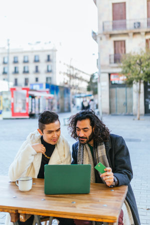Gay couple shopping online using laptop and credit card outdoors