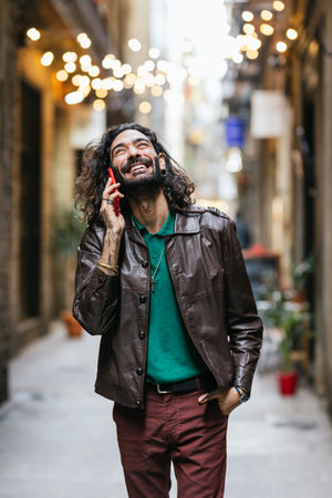 Stylish man laughing while talking on phone in city alleyの写真素材